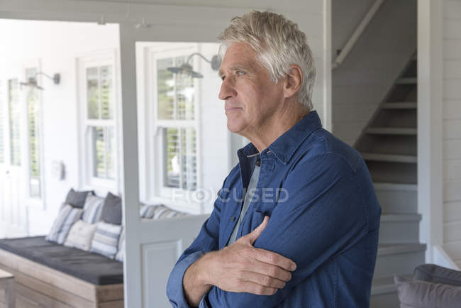 Uomo anziano premuroso in piedi a casa e guardando altrove — Foto stock