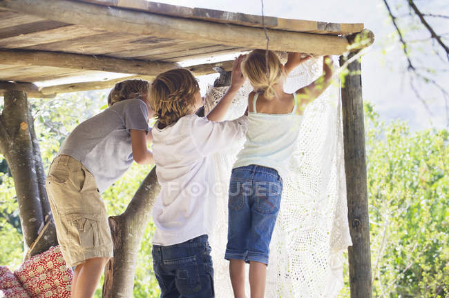 Bambini che appendono la tenda nella casa sull'albero nel giardino estivo — Foto stock