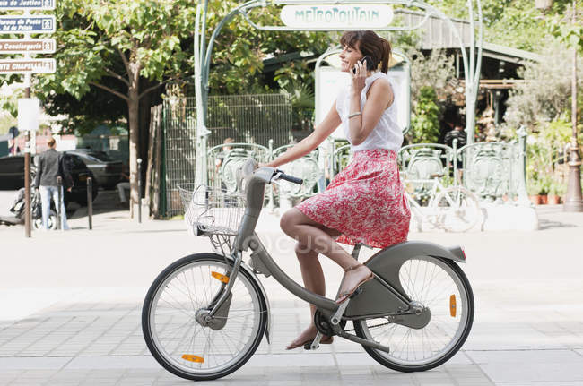 Mujer montando bicicleta y hablando por teléfono móvil, París, Ile-de-France, Francia - foto de stock