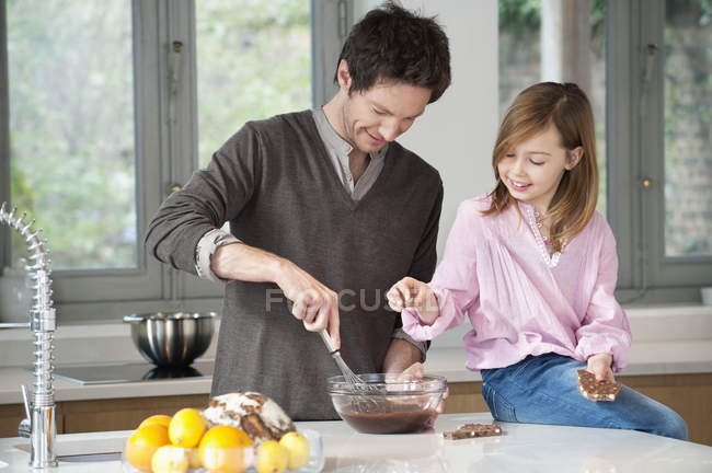 Людина перемішування суміші в миску з дочкою в кухні — стокове фото