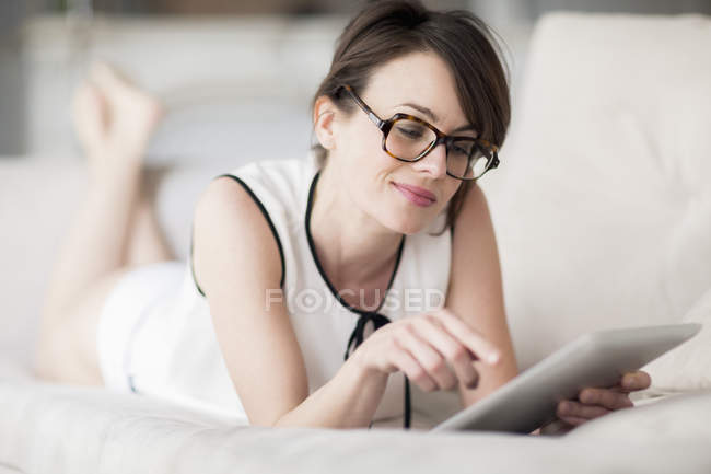 Mulher sorridente deitada na cama e usando tablet digital — Fotografia de Stock