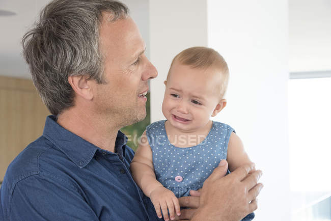 Femmina bambino piangendo tra le braccia del padre a casa — Foto stock