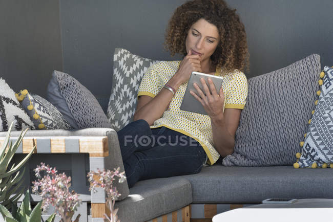 Женщина сидит на диване дома и с помощью цифрового планшета — стоковое фото