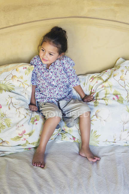 Linda niña sentada en almohadas en la cama - foto de stock