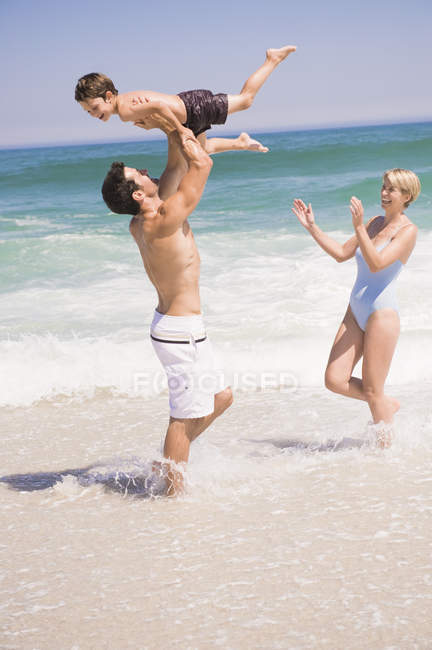 Familia alegre jugando en la playa de arena - foto de stock