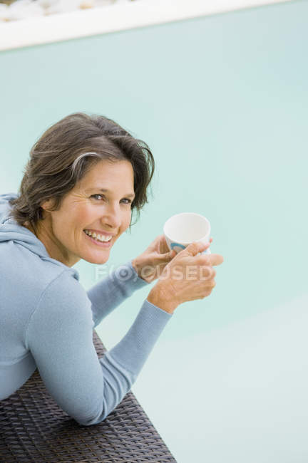 Усміхнена жінка тримає чашку чаю біля басейну — стокове фото