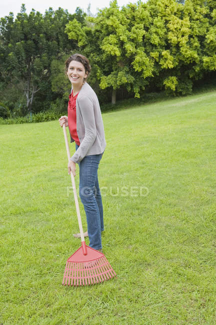 Retrato de mulher sorrindo raking gramado verde — Fotografia de Stock