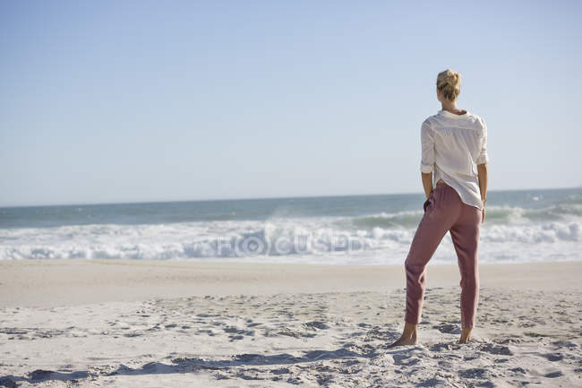 Visão traseira da jovem mulher magro em pé na praia ensolarada — Fotografia de Stock