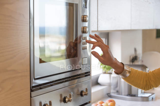 Close-up of female hand pushing button of oven in kitchen — Stock Photo