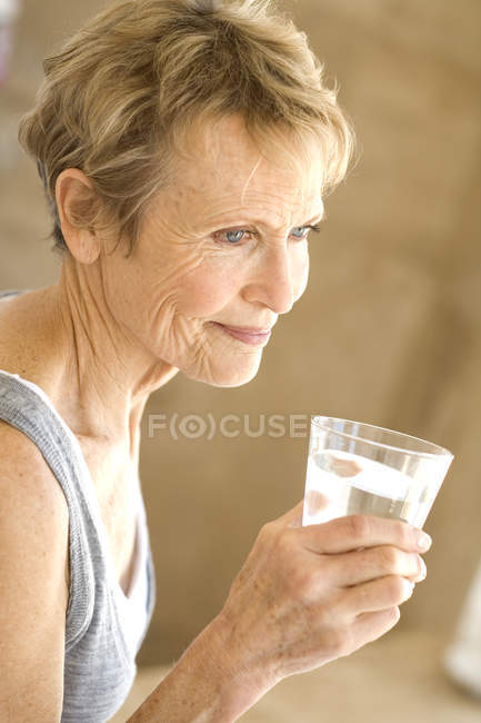 Portrait of senior woman with short hair holding glass of water — Stock Photo