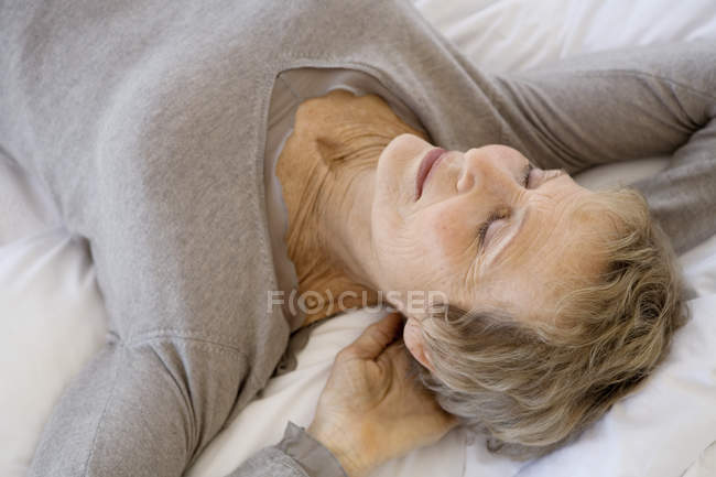 Entspannte Seniorin liegt mit den Händen hinter dem Kopf auf dem Bett — Stockfoto