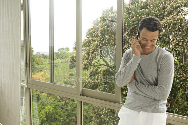 Улыбающийся мужчина звонит, опираясь на окно в саду — стоковое фото
