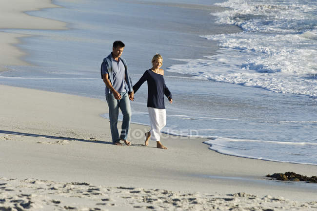Пара держащихся за руки, гуляющих по песчаному пляжу — стоковое фото