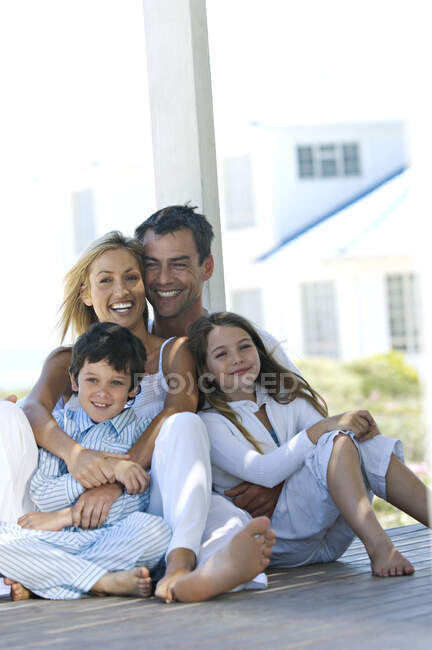 Casal e duas crianças sorrindo para a câmera, sentado no terraço de madeira — Fotografia de Stock