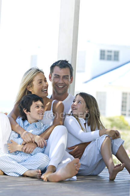 Coppia e due figli sorridenti per la macchina fotografica, seduti sulla terrazza in legno — Foto stock