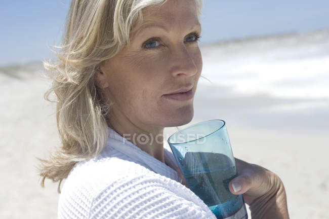 Portrait de femme réfléchie sur la plage tenant un verre d'eau — Photo de stock