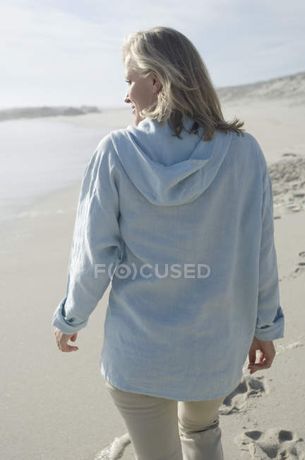 Женщина идет по песчаному пляжу и смотрит в сторону — стоковое фото