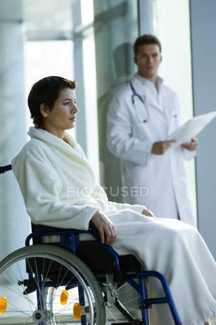 Female patient sitting in wheelchair and male doctor standing on background in hospital — Stock Photo