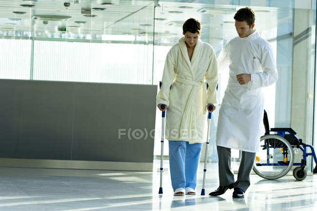 Врач-мужчина помогает пациентке ходить на костылях в больнице — стоковое фото