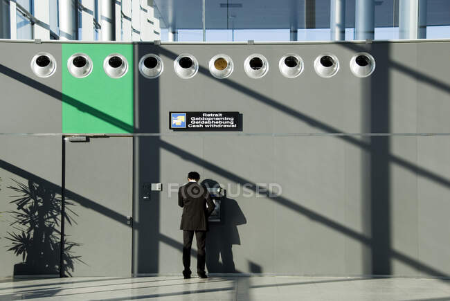 Hombre usando cajero automático en el aeropuerto, vista trasera - foto de stock