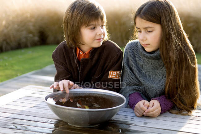 Dos niños pensando delante de un tazón de agua - foto de stock