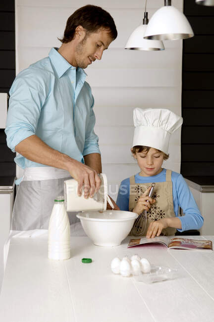 Середній дорослий чоловік робить торт зі своїм сином на кухні — стокове фото