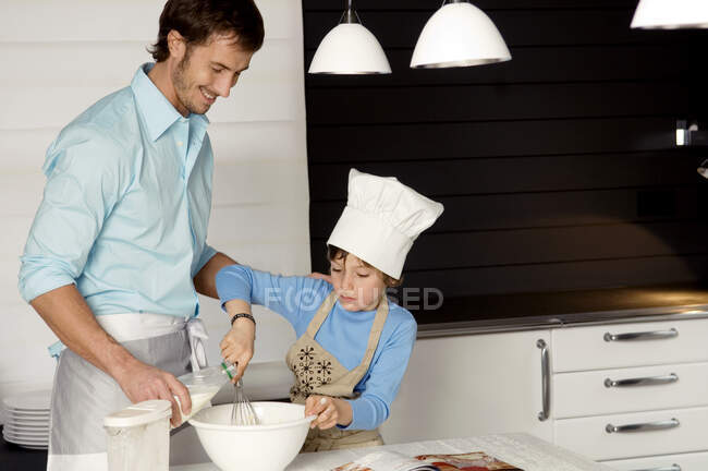 Mid adulte homme faire un gâteau avec son fils dans la cuisine — Photo de stock