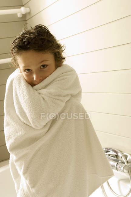 Portrait de petit garçon enveloppé dans une serviette debout dans la salle de bain — Photo de stock