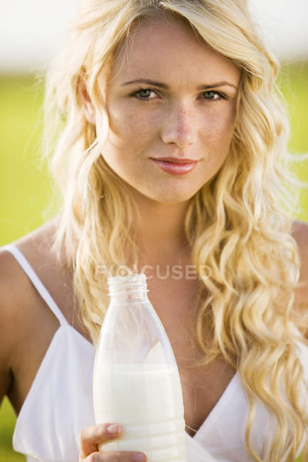 Portrait de jeune femme tenant une bouteille de lait à l'extérieur — Photo de stock
