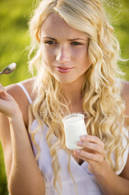 Porträt einer jungen blonden Frau, die im Freien Joghurt isst — Stockfoto