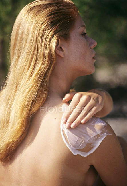 Naked young woman applying sun cream on shoulder outdoors — Stock Photo