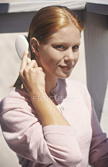 Porträt einer lächelnden jungen rothaarigen Frau, die sich im Freien die Haare bürstet — Stockfoto