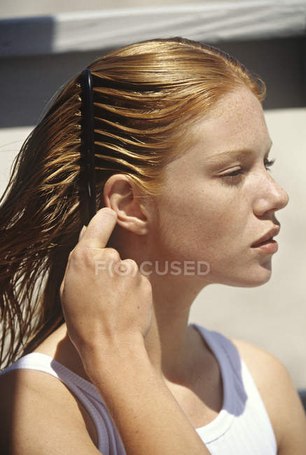 Mujer pelirroja joven cepillando el cabello al aire libre - foto de stock