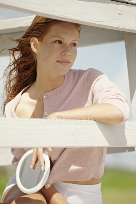 Mujer pelirroja joven sentada en el balcón y mirando a la vista - foto de stock