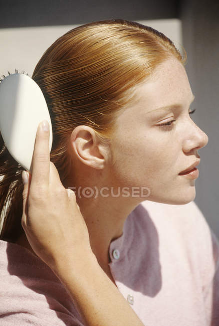 Jeune femme rousse brossant les cheveux à l'extérieur — Photo de stock