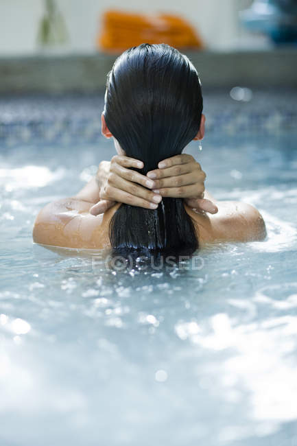 Vista trasera de la mujer tocando el cabello mojado en la piscina - foto de stock