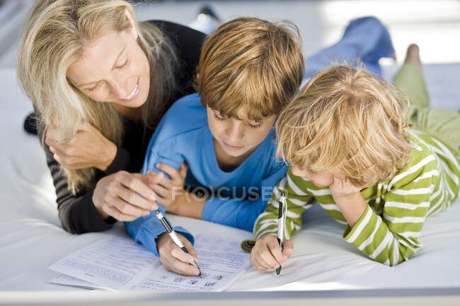Femme aidant ses fils dans leurs devoirs — Photo de stock