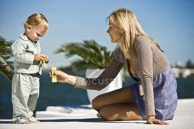 Mulher segurando uma garrafa de bolha de sabão na frente de seu filho — Fotografia de Stock
