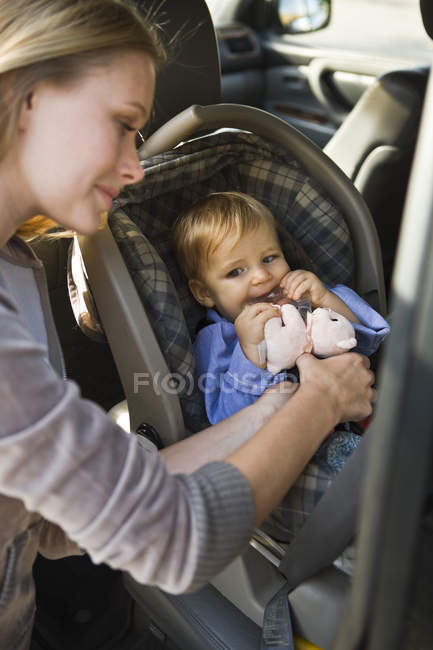 Женщина прикрепляет маленького сына к детскому креслу в машине — стоковое фото