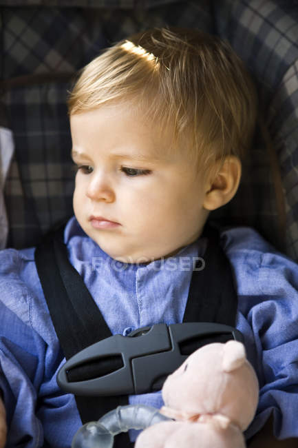 Задумчивый мальчик сидит в детском кресле — стоковое фото