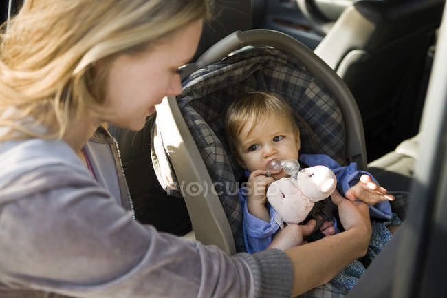 Woman fastening little son on baby seat in car — Stock Photo