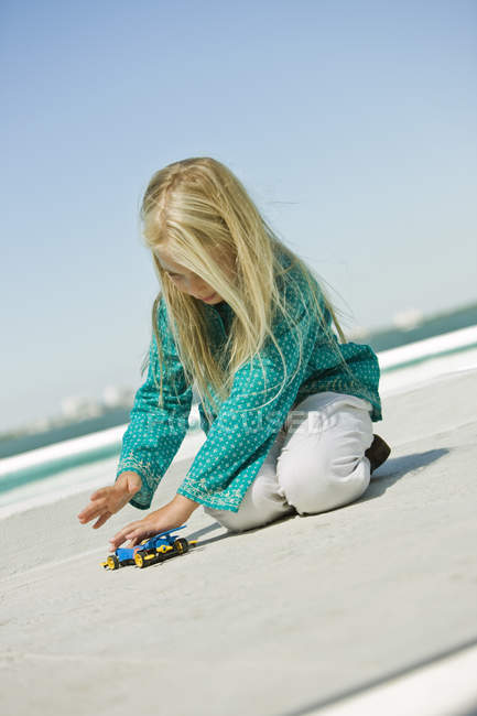 Дівчина грає з машиною з дистанційним керуванням на піщаному пляжі — стокове фото