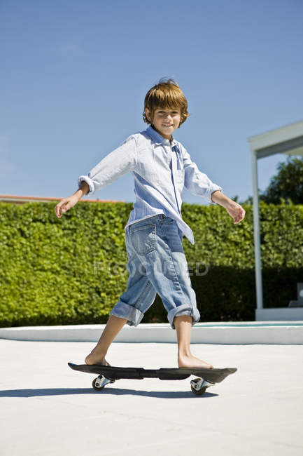 Smiling boy skateboarding in summer backyard — Stock Photo