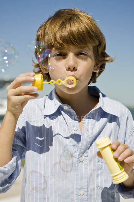 Portrait of boy blowing bubbles with bubble wand against blue sky — Stock Photo