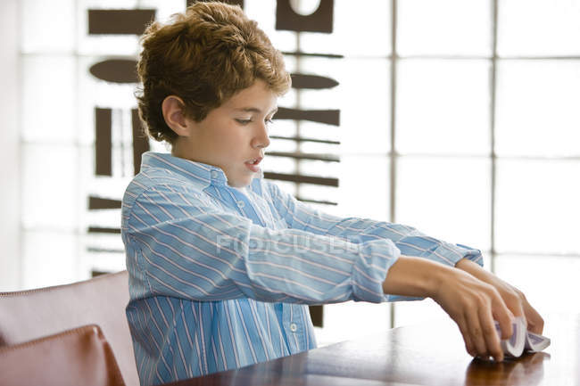 Niño enfocado barajar tarjetas en la mesa en casa - foto de stock