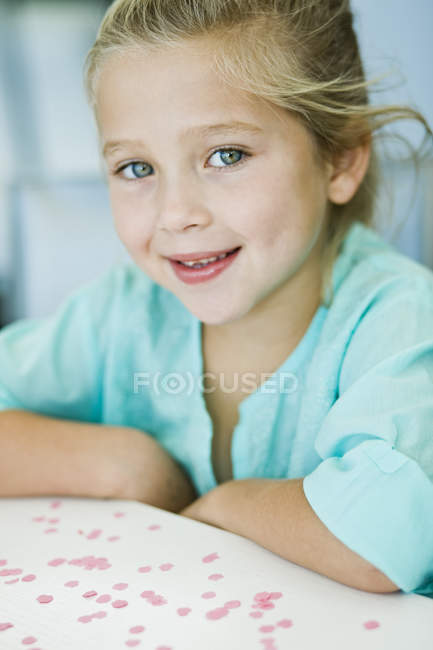 Retrato de una niña sonriente sentada en el escritorio - foto de stock