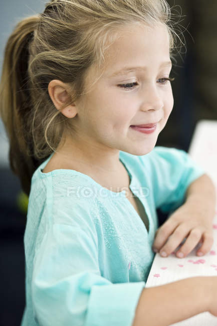 Primer plano de la niña sonriendo mientras está de pie en el escritorio - foto de stock