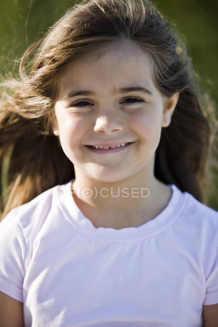 Ritratto di sorridente bambina bruna che guarda la macchina fotografica su sfondo sfocato — Foto stock