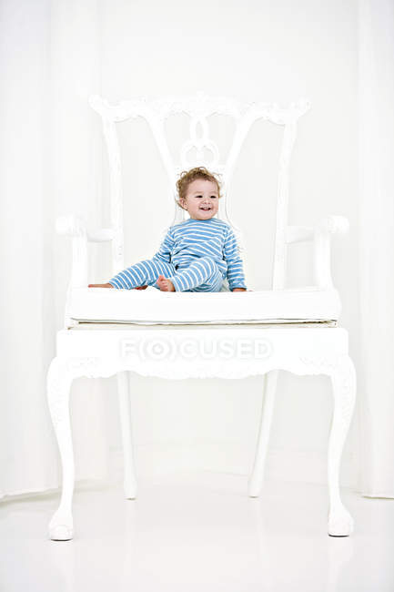 Smiling baby boy sitting in huge white armchair — Stock Photo
