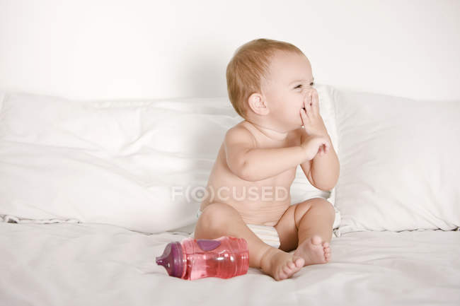 Bébé fille rire sur le lit avec bouteille — Photo de stock